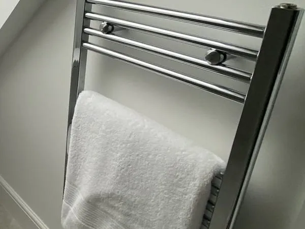 A fresh white towel folded over a chrome towel rail